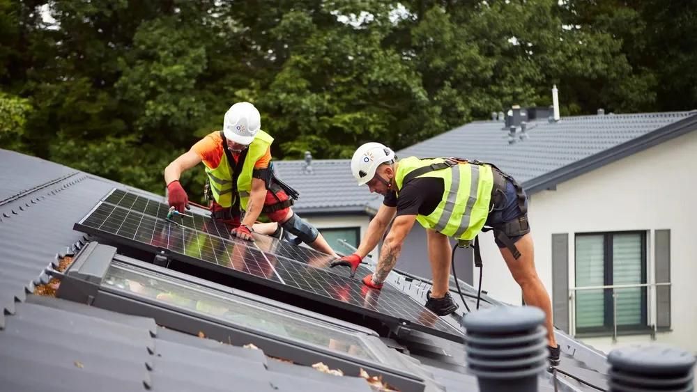 Dos instaladores solares en el tejado de una casa, trabajando en módulos solares.