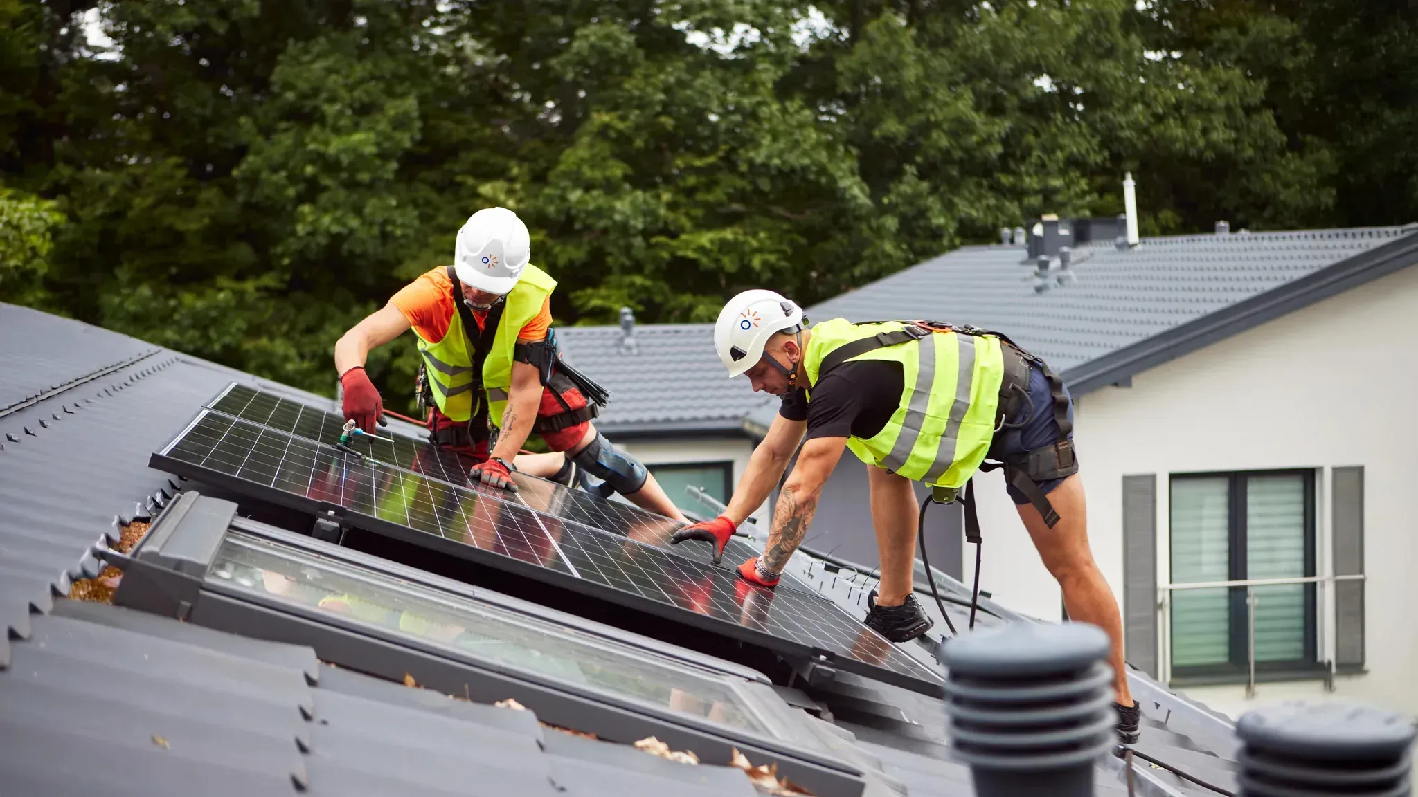 Two solar installers on the roof of a house, working on solar modules.
